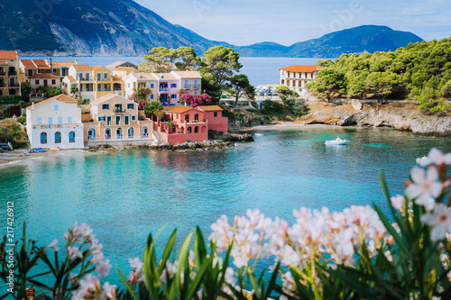 Bright white flower blossom in front of turquoise colored bay in Mediterranean sea and beautiful colorful houses in Assos village in Kefalonia, Greece