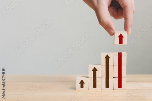Hand arranging wood block stacking as step stair with arrow up. Ladder career path concept for business growth success process