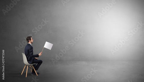 Businessman staying in an empty grey dark room with stuffs on his lap 