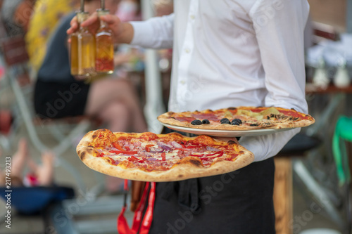 Italienischer Kellner bedient auf der Terrasse mit zwei Pizza in der Hand 