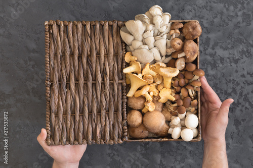 View from above of wicker basket with forest rare delicious edible mushrooms on a dark textural background, flat lay.