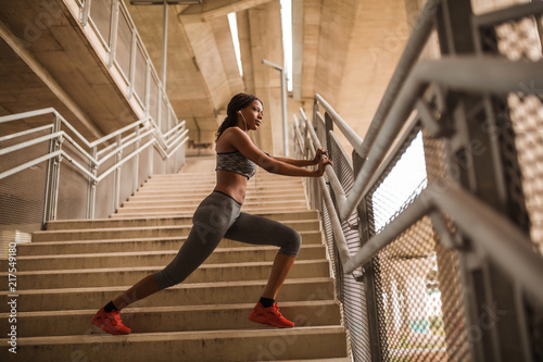 Young black athletic girl doing stretching exercise on stairs