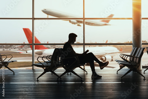 Young man sitting at airport and reding his book while waiting landing.