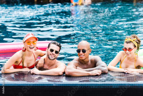 smiling friends in sunglasses resting in swimming pool