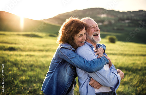 Side view of senior couple hugging outside in spring nature at sunset.