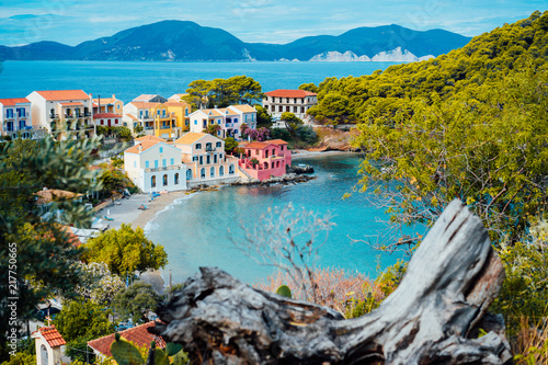 Assos village in Kefalonia, Greece. Calm blue bay water and colored traditional houses. Old snag in the front