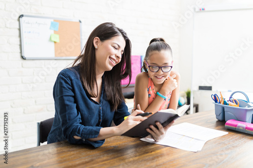 Confident Mother Reading Book To Girl At Table