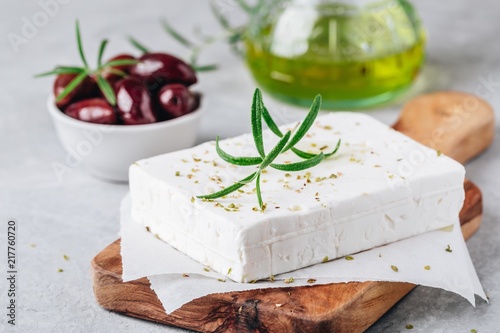 Homemade greek cheese feta with rosemary and herbs on cutting board with olive oil and olives