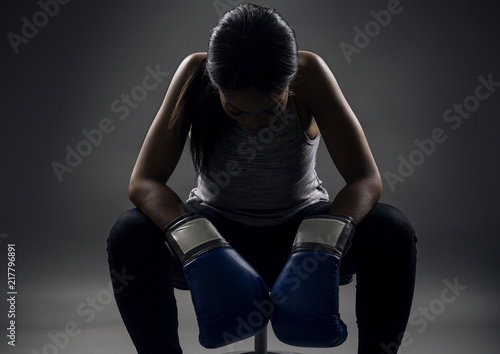 Black female wearing boxing gloves looking angry as a boxer, MMA fighter or self defense trainer sitting after working out. She is portraying female strength and determination.