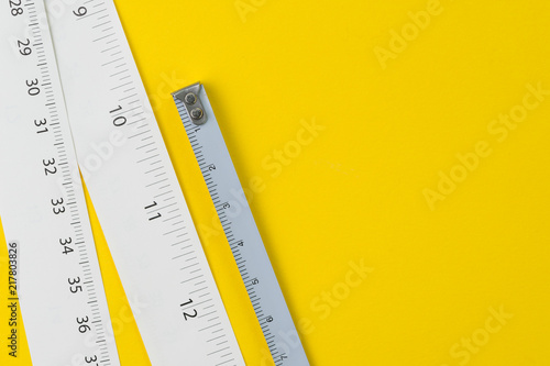 White measuring tapes with centimetre and inches on vivid yellow background with copy space, length, long or maker concept