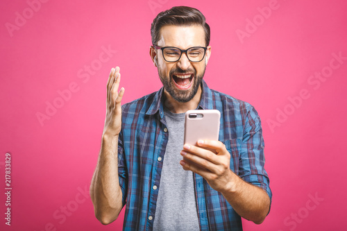 I'm a winner! Happy man holding smartphone and celebrating his success over pink background.