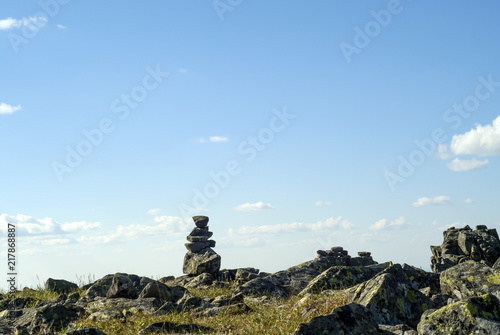 bright landscape of a high-altitude plateau with folded travelers pyramid cairn of stones under a blue sky with clouds