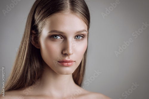 Portrait of a beautiful young girl with nude make-up in studio on a gray background