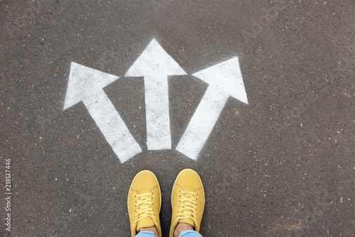 Woman standing near arrows on asphalt, top view. Choice concept