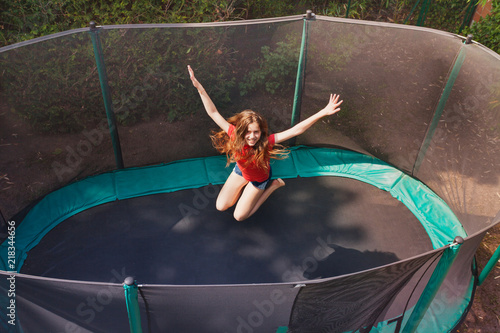 Happy teenage girl jumping on trampoline outdoors