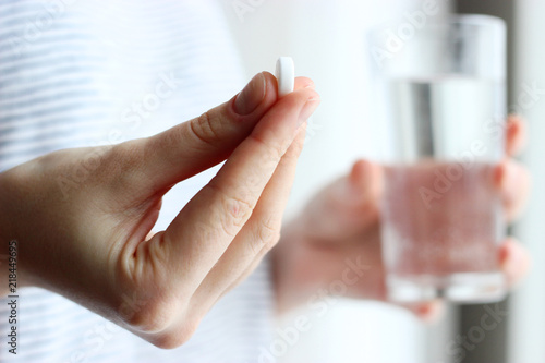 white pill and a glass of water in female hands. health concept