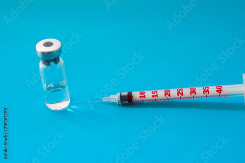 Transparent vial container with liquid medicine near small insulin syringe with capacity 1 CC and small needle on blue background. Concept of preparation for vaccination, subcutaneous administration