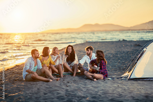 Happy friends with guitar at beach. friends relaxing on sand at beach with guitar and singing on summer sunset.