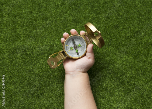 compass in hand on a background of green artificial grass, travel, tourism, outdoor activities.