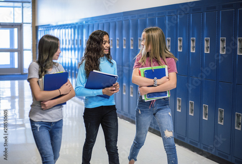 Candid photo of Three Junior High school Students talking together in a school hallway. Diverse Female school girls smiling and having fun together during a break at school