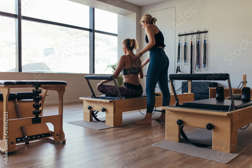 Trainer guiding a pilates woman for correct posture at the gym