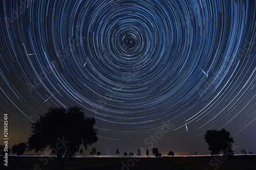 Night landscape with trees, lights of passing cars and startrails in the sky and falling stars - perseids