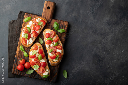 Bruschetta with tomatoes, mozzarella cheese and basil on a cutting board. Traditional italian appetizer or snack, antipasto. Top view with copy space. Flat lay