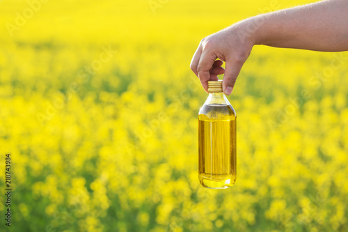 rapeseed oil in bottle in hand on background rape field