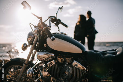 selective focus of classical chopper motorbike and couple looking at sea on background