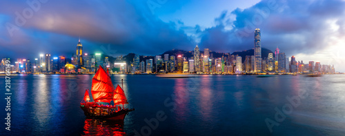 Panorama of Hong Kong City skyline with tourist sailboat at night. View from across Victoria Harbor HongKong.