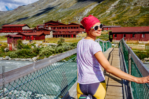 Sportive female tourist standing on bridge above river enjoying landscape in Jotunheimen national park Norway Travel scandinavian scenery.