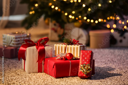 Beautiful Christmas gift boxes on floor near fir tree in room