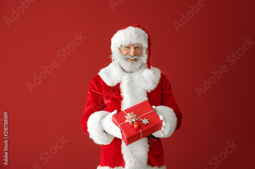 Santa Claus with gift box on color background