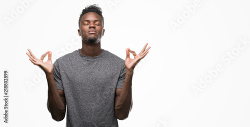 Young african american man wearing grey t-shirt relax and smiling with eyes closed doing meditation gesture with fingers. Yoga concept.
