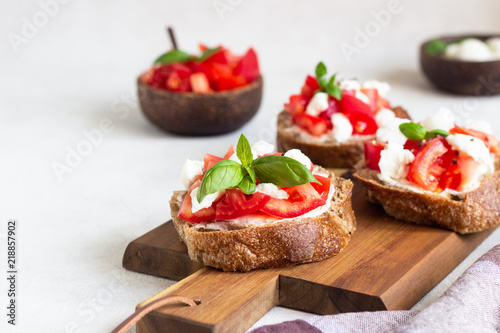 Italian bruschetta with chopped cherry tomatoes, mozzarella cheese and basil on wooden cutting board. 