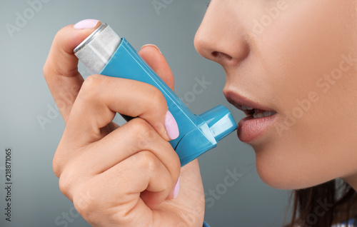 Young woman using asthma inhaler on color background, closeup