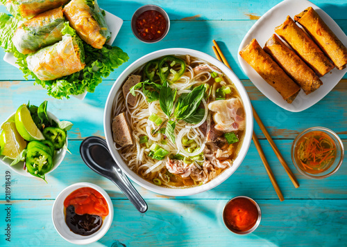 vietnamese beef pho bo soup in bowl on table top with spring rolls and appetizers