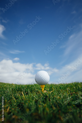 golf ball on tee, green grass and blue sky background