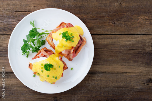 Eggs benedict with bacon on wooden background . Top view 
