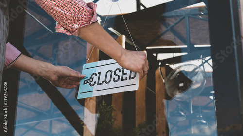 Caucasian female turning sign from open to closed on the entrance door of his small cafe. Out of business