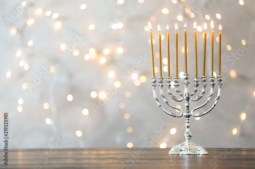 Hanukkah menorah with candles on table against blurred lights