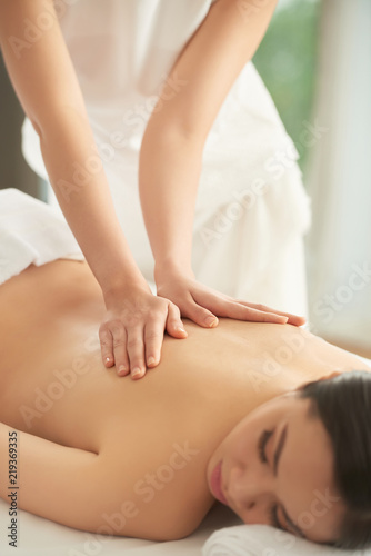 Young Asian woman enjoying back massage in spa salon