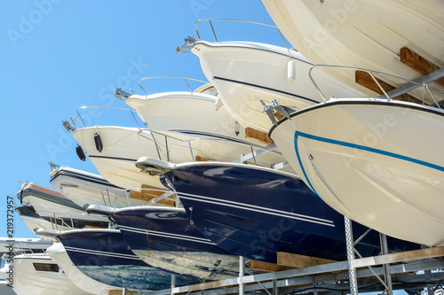 View from below of the hulls of motorboats racked one above another on two levels in a dry rack boat storage facility against blue sky.