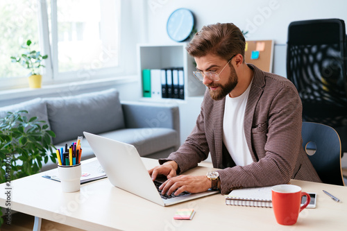 Young startup entrepreneur working on laptop in modern home office. Portrait of businessman during work