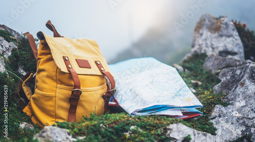 Hipster hiker tourist yellow backpack and map europe on background green grass nature in mountain, blurred panoramic landscape, traveler relax holiday concept, view planning wayroad in trip vacation