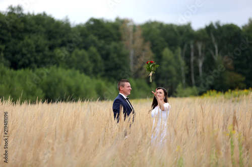 Młoda para na łące łapie bukiet ślubny z czerwonych róż.