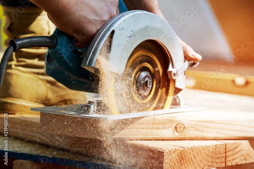 Building contractor worker using hand held worm drive circular saw to cut boards on a new home constructiion project