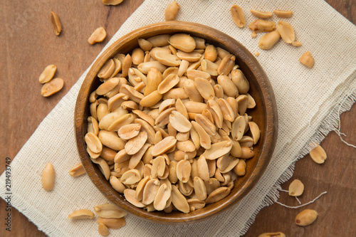 Roasted peanuts in wooden bowl putting on linen and wooden background.