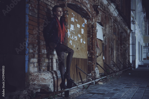 A sexy girl stands under a lantern and poses in the image of a seductive prostitute. The concept of selling love.. Woman in a dark with a cigar, it looking sad eyes down.