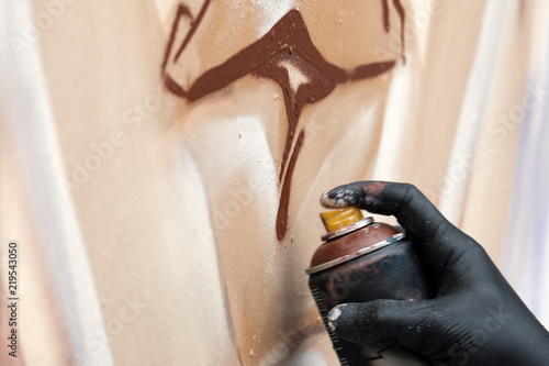 A street artist in black gloves draws an abstract image using a brown spray paint. Graffiti concept. Close-up of a hand with a ballon.